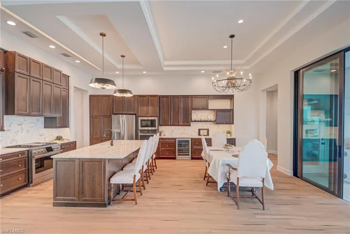 Kitchen with appliances with stainless steel finishes, hanging light fixtures, a kitchen island with sink, a breakfast bar area, and light stone counters