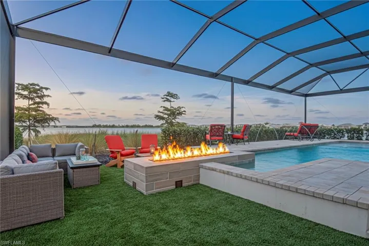 Pool at dusk featuring a patio, a water view, a sunroom, and a yard