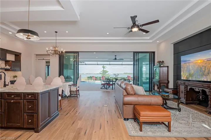 Living room with a ceiling fan, light wood-style flooring, a tray ceiling, a chandelier, and recessed lighting