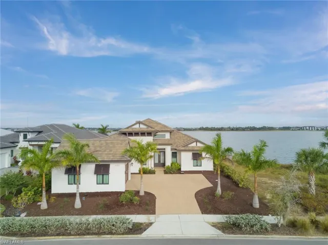 View of front facade with decorative driveway, stucco siding, a shingled roof, and a water view