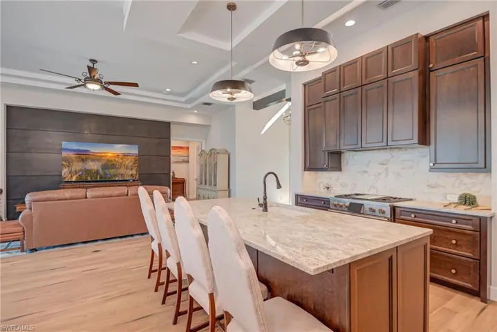 Kitchen featuring a breakfast bar area, open floor plan, light stone counters, light wood finished floors, and an island with sink