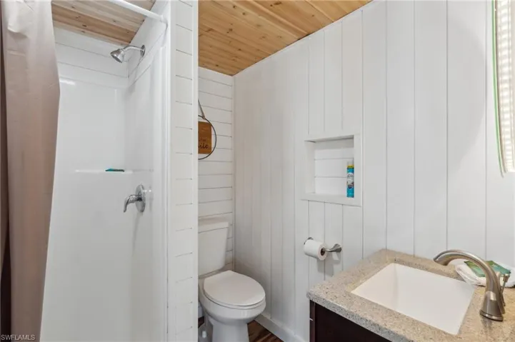 Bathroom with toilet, vanity, wood walls, wooden ceiling, and a shower with shower curtain