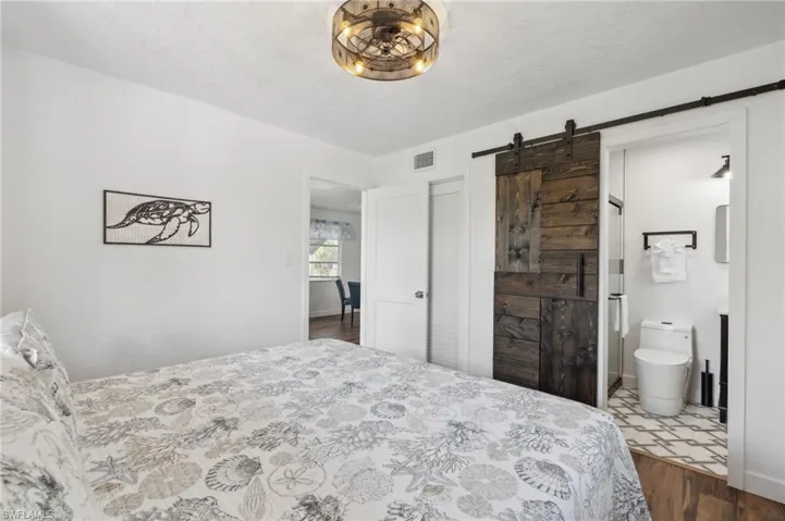 Bedroom with a textured ceiling, wood-type flooring, ensuite bathroom, and a barn door