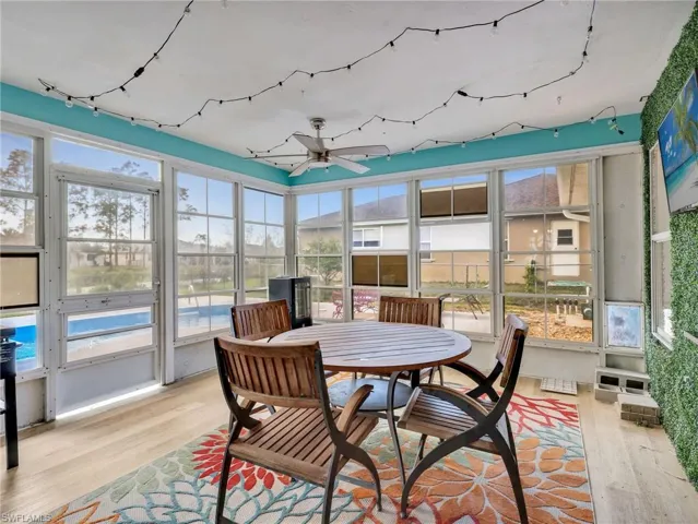 Sunroom featuring abundant natural light, wood-finish flooring, a ceiling fan, and a vibrant accent wall