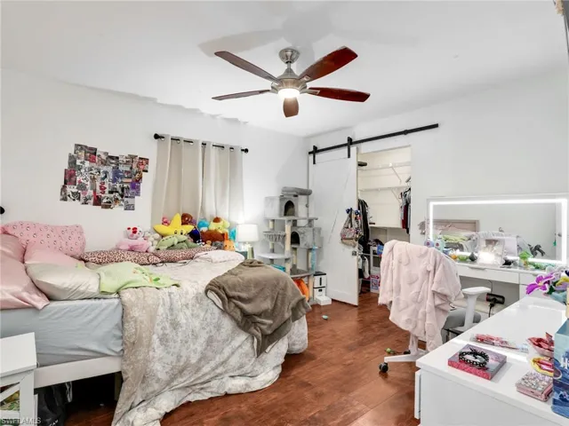 Bedroom featuring wood-finish flooring, a ceiling fan with light fixture, and a white barn door leading to a closet with wire shelving