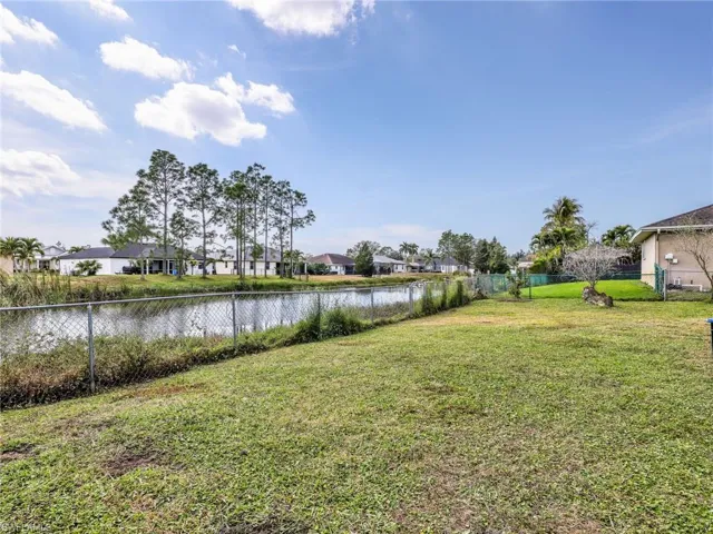 Expansive backyard featuring a lush lawn, chain-link fencing, and serene water frontage