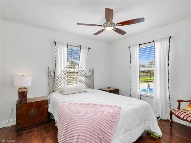 Back secondary bedroom bright interior space featuring wood-finish flooring, a ceiling fan with integrated lighting, and two windows with white blinds