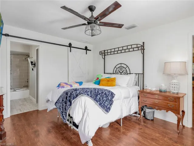 Spacious room featuring wood-finish flooring, a contemporary ceiling fan with integrated lighting, and a white barn door
