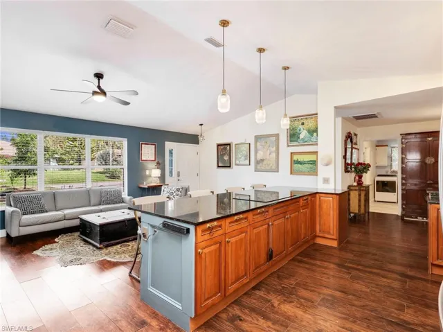 Kitchen island with dark countertop and wood-finish cabinetry, illuminated by three pendant lights