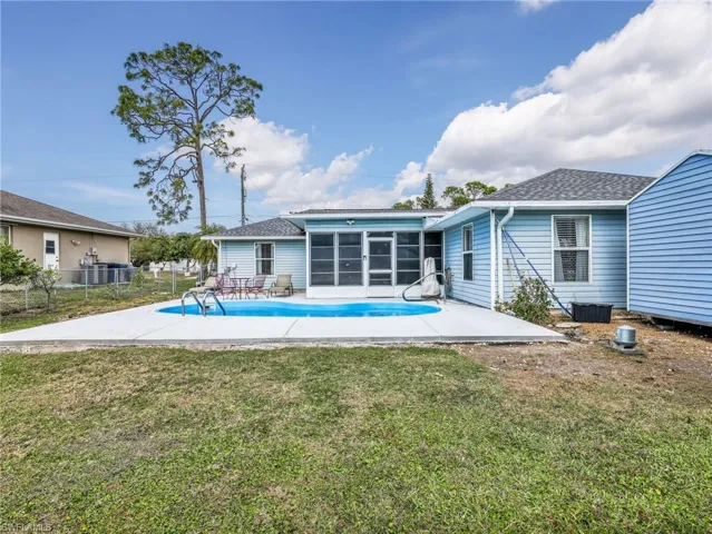 Backyard pool area featuring a kidney-shaped pool, concrete surround, screened patio enclosure, and blue horizontal siding