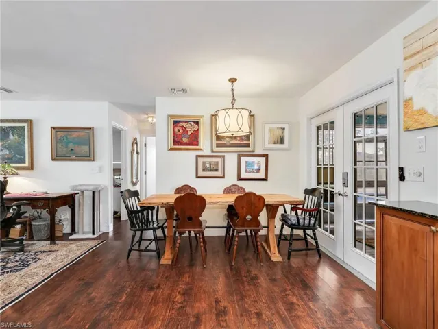 Spacious dining area featuring wood-finish flooring, a decorative chandelier, and white paneled French doors