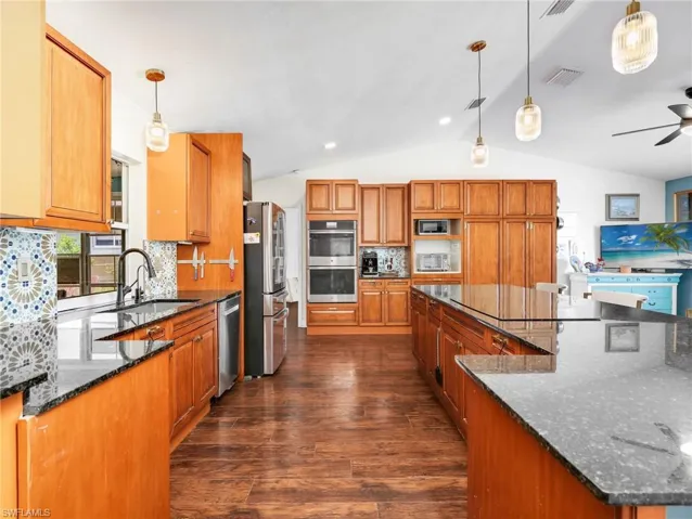 Spacious kitchen featuring extensive wood cabinetry, dark granite countertops, stainless steel appliances, a patterned tile backsplash, and wood-finish flooring