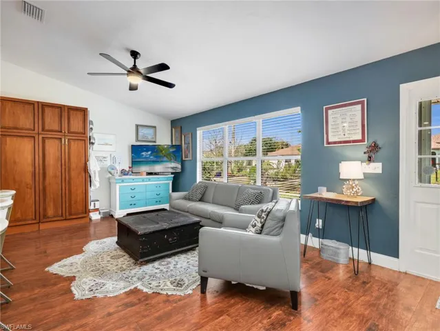 Spacious living area featuring rich wood-finish flooring, a vaulted ceiling, and a prominent window offering abundant light
