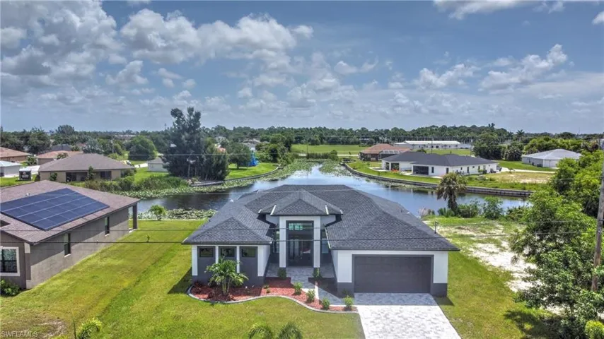 View of front of home featuring a garage, a water view, a front lawn, and solar panels