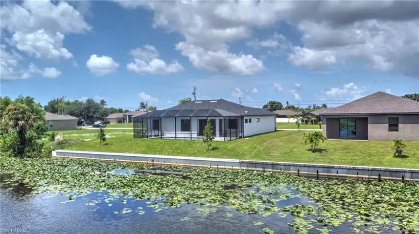 Back of house with glass enclosure and a lawn
