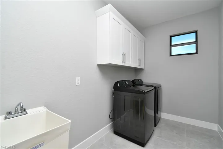 Clothes washing area featuring sink, cabinets, washing machine and dryer, and light tile patterned floors