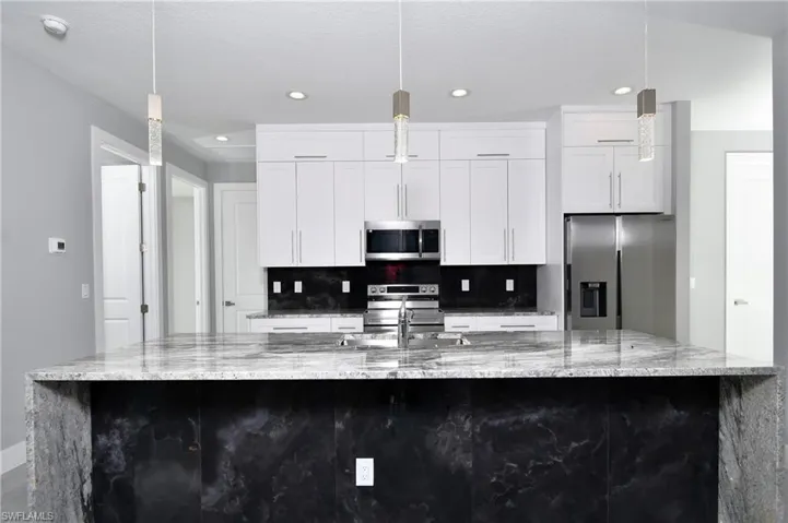 Kitchen with white cabinetry, appliances with stainless steel finishes, light stone countertops, and a large island with sink