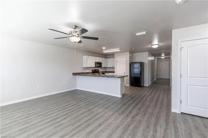 Kitchen featuring a peninsula, black appliances, white cabinets, open floor plan, and ceiling fan