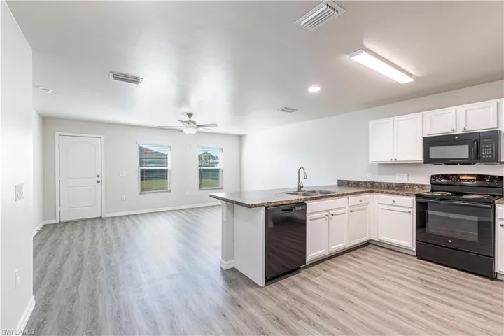 Kitchen with black appliances, dark countertops, a peninsula, white cabinetry, and light wood finished floors