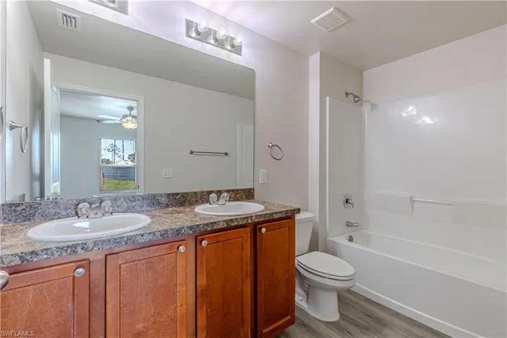 Bathroom featuring double vanity, light wood-style flooring, washtub / shower combination, and ceiling fan