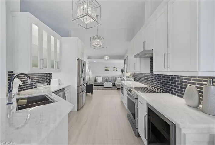 Kitchen featuring decorative backsplash, open floor plan, stainless steel appliances, and light stone countertops
