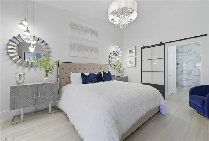 Bedroom with a barn door, connected bathroom, wood finished floors, a high ceiling, and a chandelier