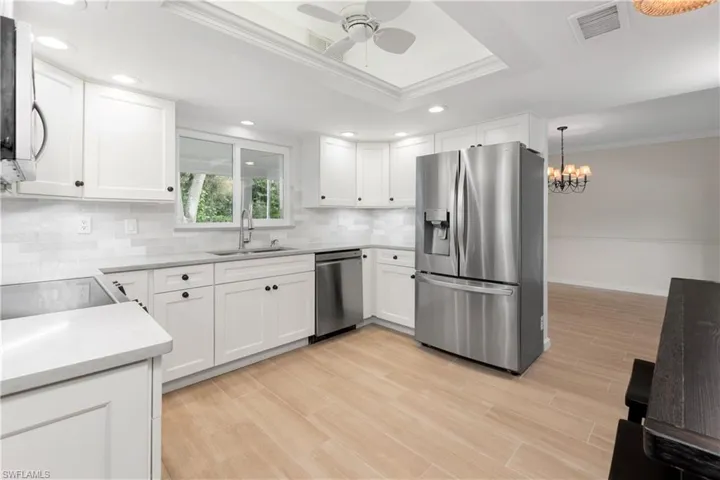 Kitchen with white cabinetry, stainless steel appliances, a raised ceiling, and sink