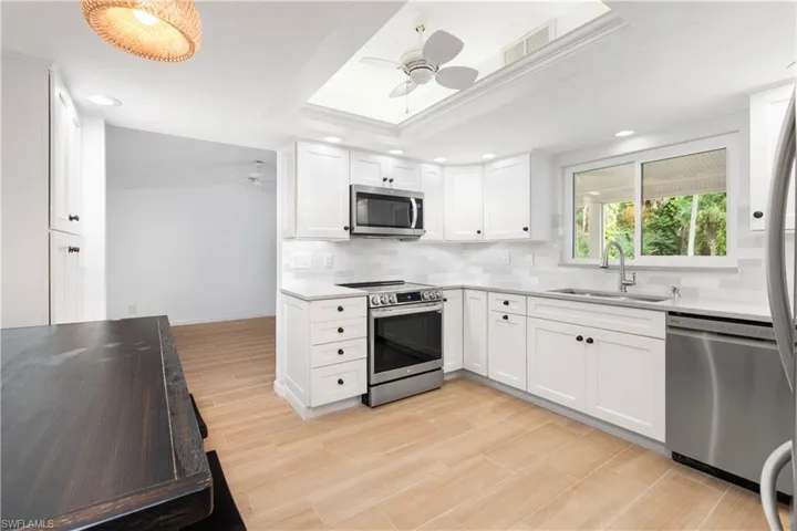 Kitchen featuring appliances with stainless steel finishes, a raised ceiling, sink, and white cabinets