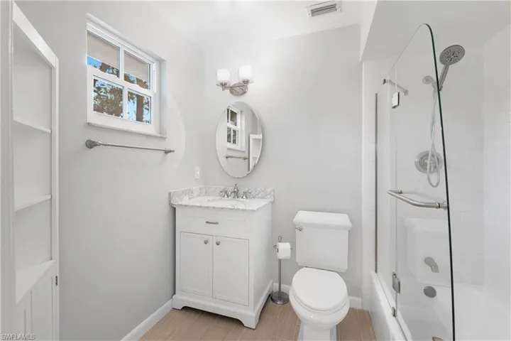 Full bathroom with enclosed tub / shower combo, vanity, and toilet