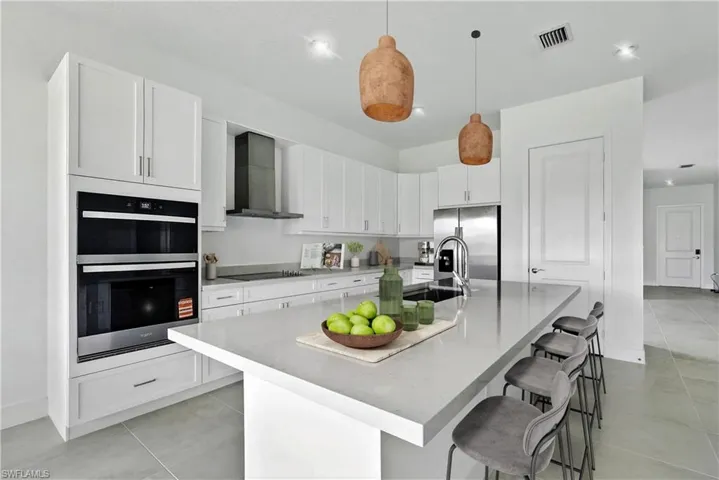 Kitchen with white cabinetry, wall chimney range hood, an island with sink, and a breakfast bar area