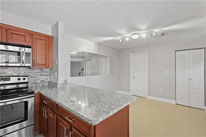 Kitchen with stainless steel appliances, decorative backsplash, light stone counters, a peninsula, and a textured ceiling