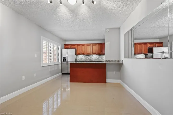 Kitchen featuring light tile patterned flooring, decorative backsplash, stainless steel refrigerator with ice dispenser, a textured ceiling, and brown cabinets
