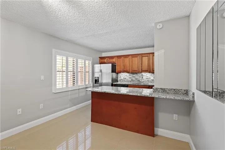 Kitchen featuring brown cabinets, light stone counters, a textured ceiling, tasteful backsplash, and light tile patterned flooring