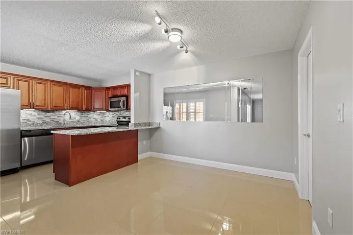 Kitchen with light stone countertops, light tile patterned flooring, stainless steel appliances, a peninsula, and tasteful backsplash