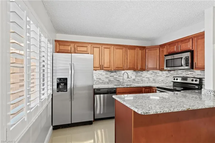 Kitchen featuring light stone countertops, appliances with stainless steel finishes, light tile patterned floors, brown cabinets, and a peninsula