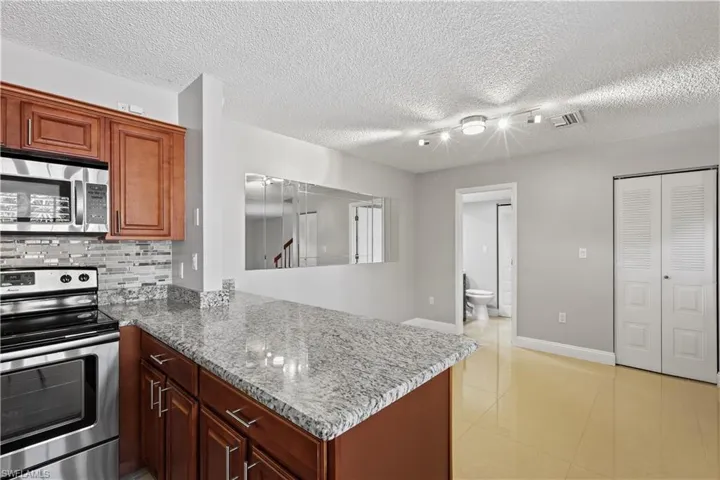 Kitchen featuring stainless steel appliances, decorative backsplash, light stone counters, a peninsula, and light tile patterned floors