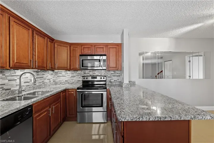 Kitchen with appliances with stainless steel finishes, light stone countertops, a peninsula, light tile patterned flooring, and tasteful backsplash