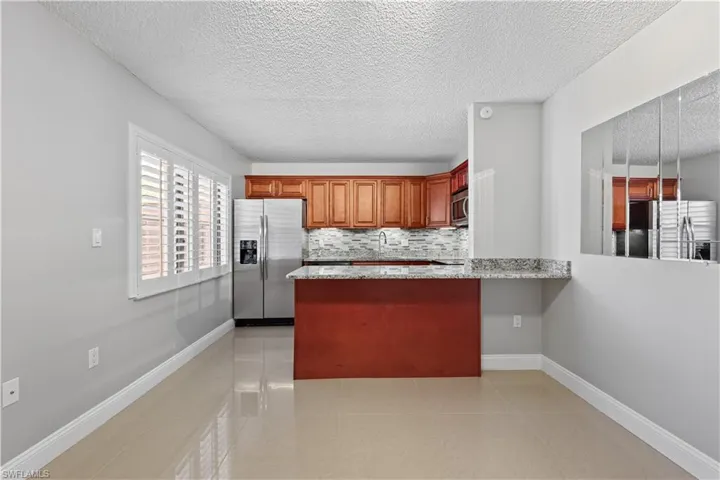 Kitchen featuring appliances with stainless steel finishes, light stone countertops, a textured ceiling, brown cabinets, and light tile patterned flooring