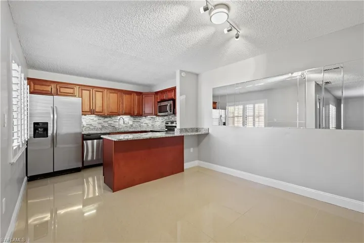Kitchen with stainless steel appliances, light stone counters, a peninsula, a textured ceiling, and backsplash