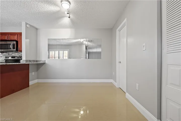 Kitchen featuring light tile patterned flooring, appliances with stainless steel finishes, decorative backsplash, a textured ceiling, and light stone counters