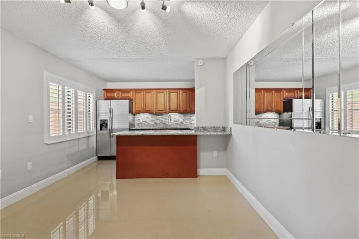 Kitchen featuring brown cabinets, stainless steel refrigerator with ice dispenser, backsplash, light tile patterned floors, and a textured ceiling