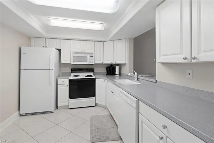 Kitchen with white cabinets, white appliances, a raised ceiling, and sink