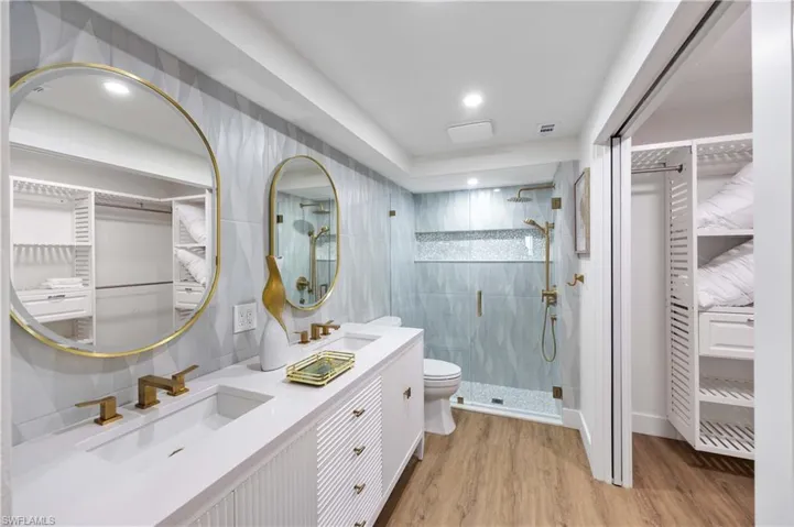 Bathroom with a shower with door, tile walls, vanity, wood-type flooring, and toilet