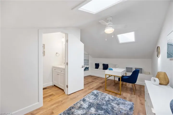 Office area featuring lofted ceiling with skylight, ceiling fan, and light wood-type flooring