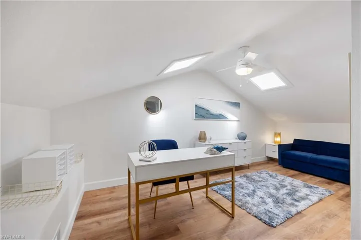 Home office with ceiling fan, lofted ceiling with skylight, and hardwood / wood-style floors