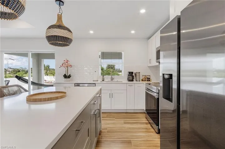 Two tone kitchen featuring stainless steel appliances, dual tone cabinetry, light wood-style flooring, backsplash, and pendant lighting