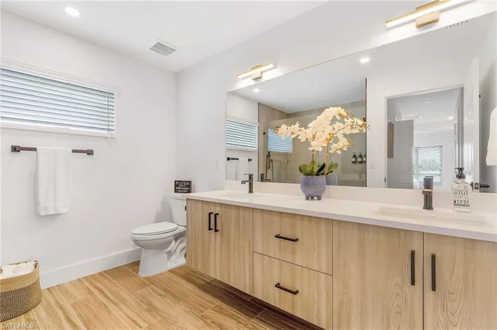 Full bathroom with double vanity, a shower stall, wood finish floors, and recessed lighting