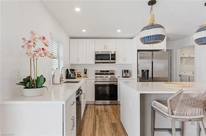 Kitchen with stainless steel appliances, a kitchen bar, light wood-type flooring, white cabinets, and light stone countertops