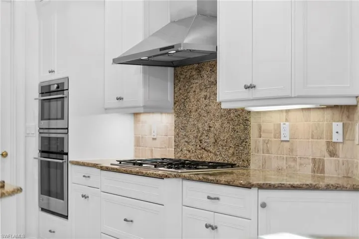 Kitchen featuring white cabinetry, wall chimney exhaust hood, stainless steel appliances, dark stone countertops, and decorative backsplash
