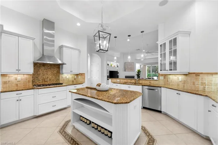 Kitchen featuring wall chimney exhaust hood, stainless steel appliances, pendant lighting, decorative backsplash, and a kitchen island